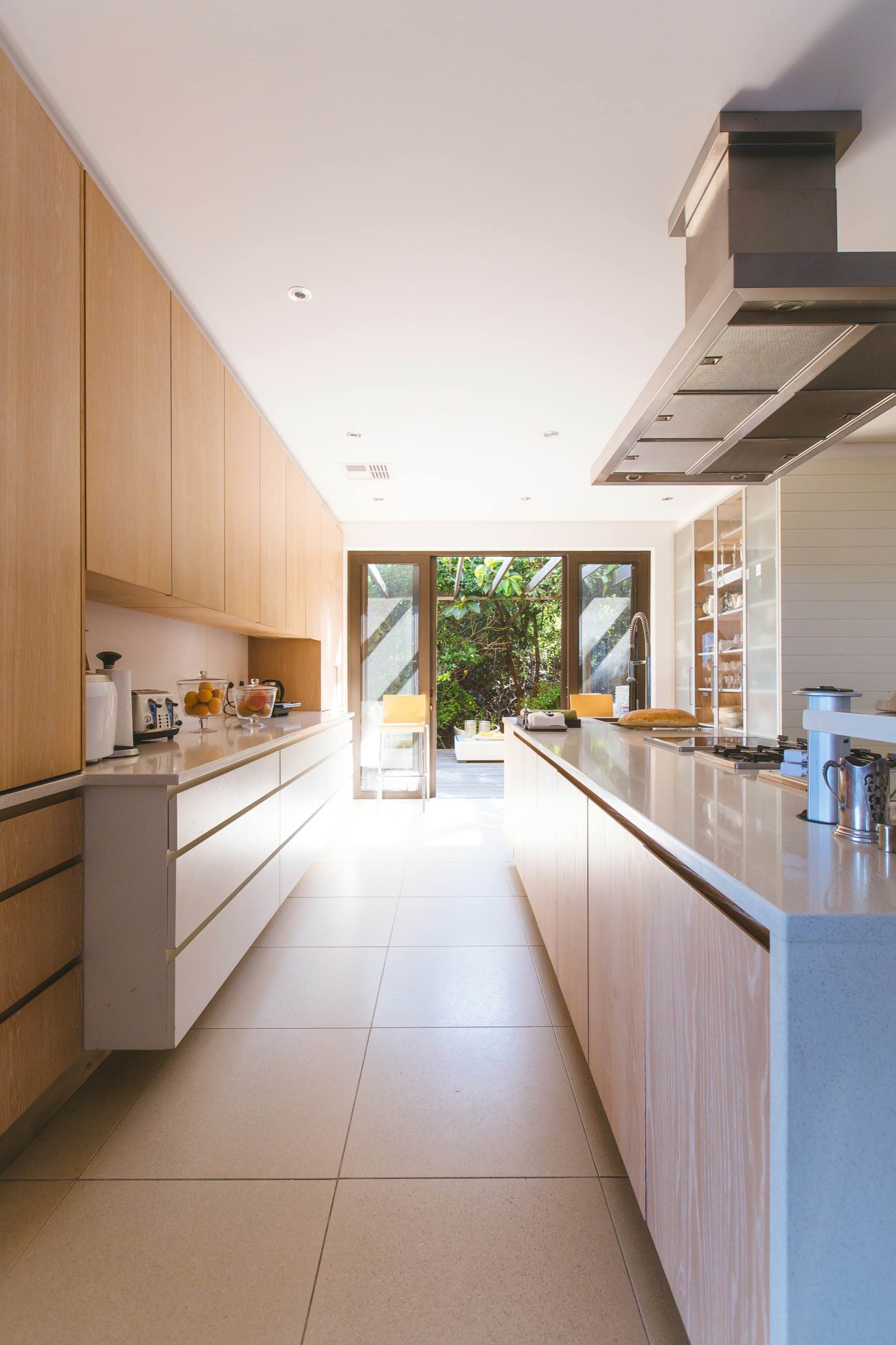 A long galley kitchen in pale wood opening onto a garden