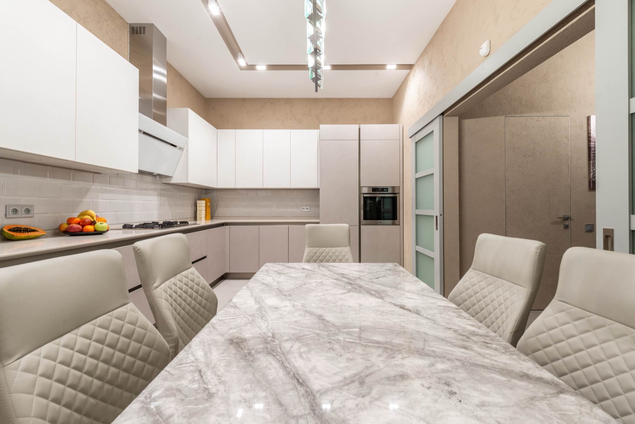 A white kitchen with a marble-topped island and quilted dining chairs