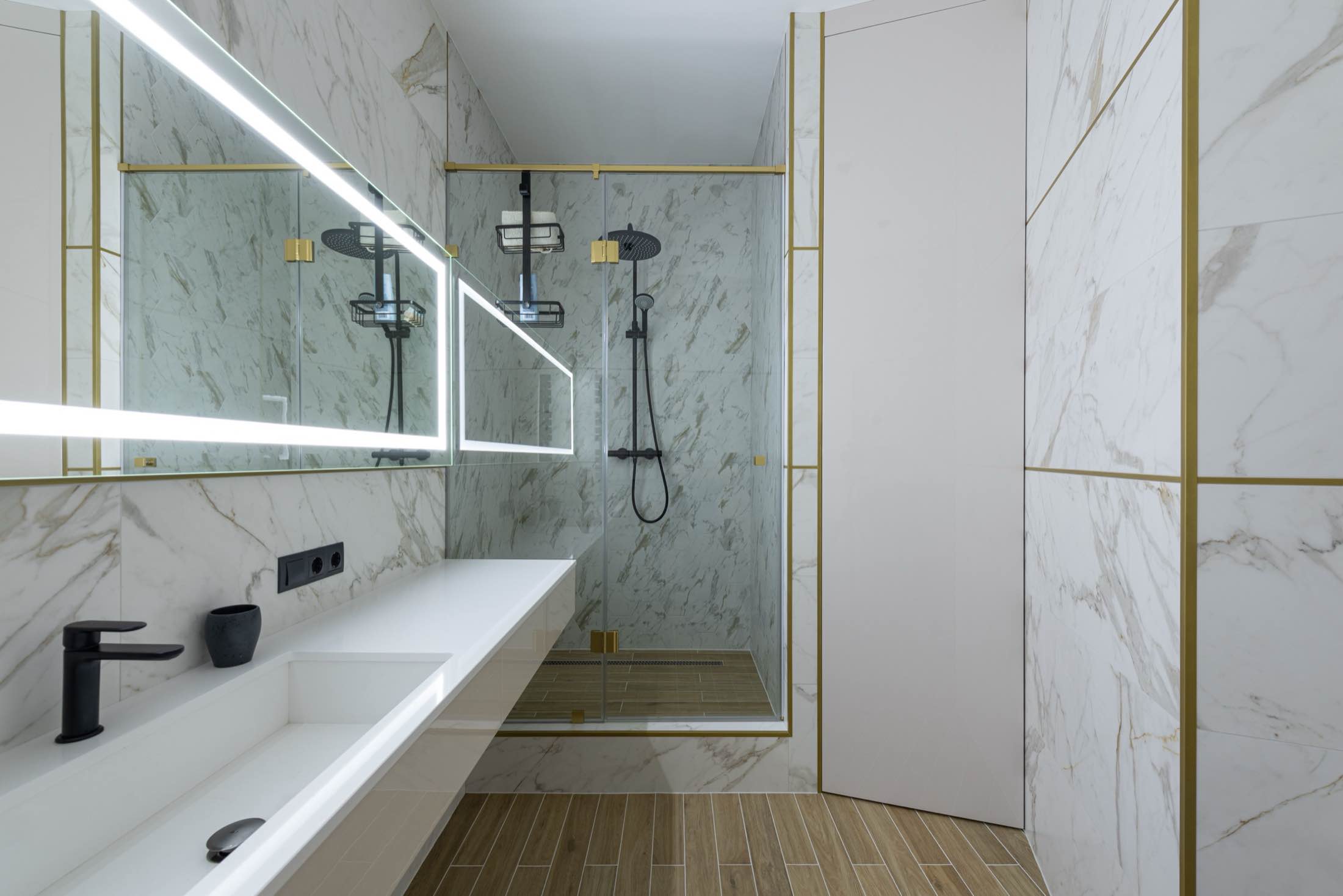 A marble walk-in shower with black fixtures and a lit mirror cabinet