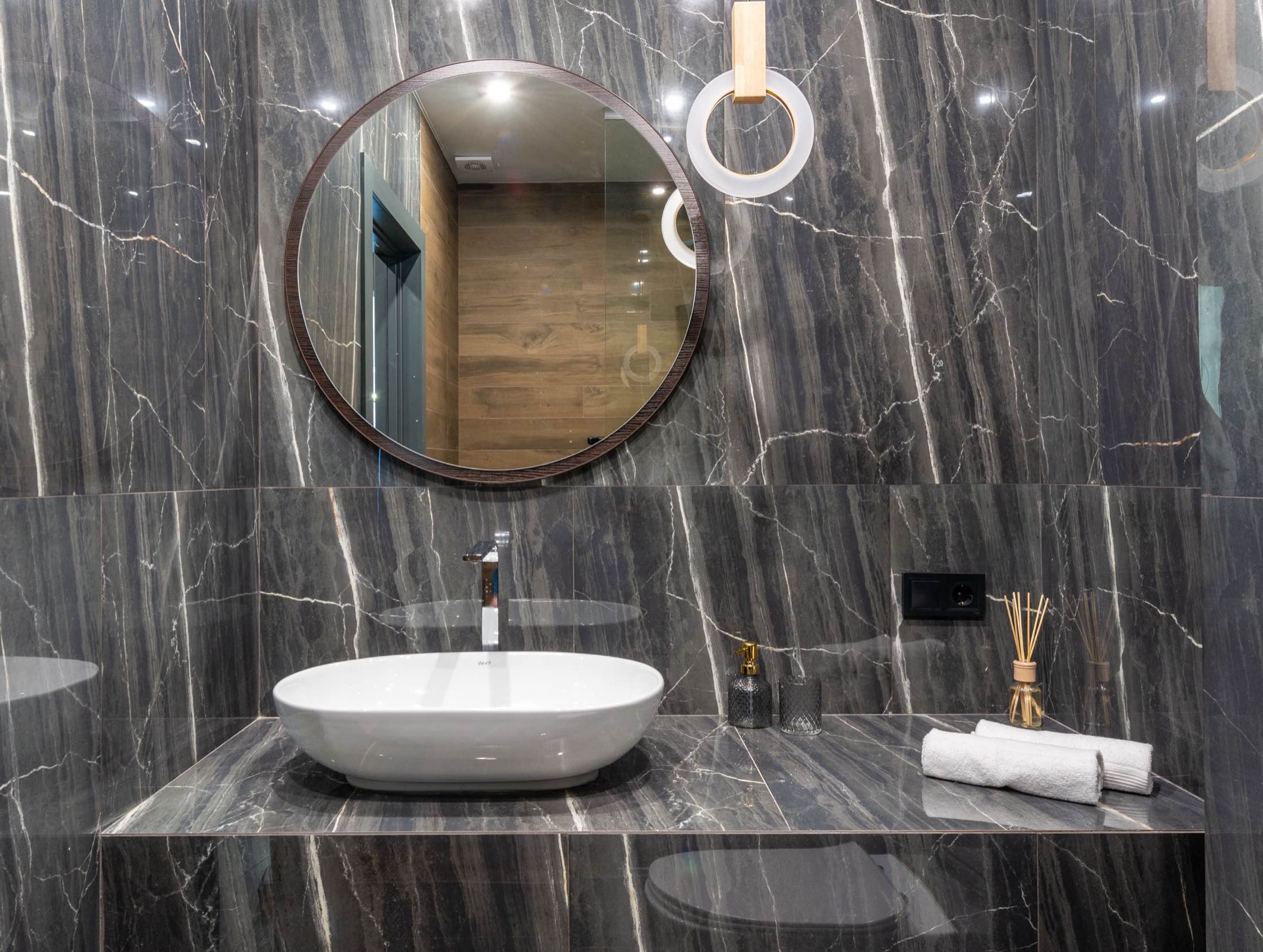 A vessel basin on a dark marble vanity beneath a round mirror