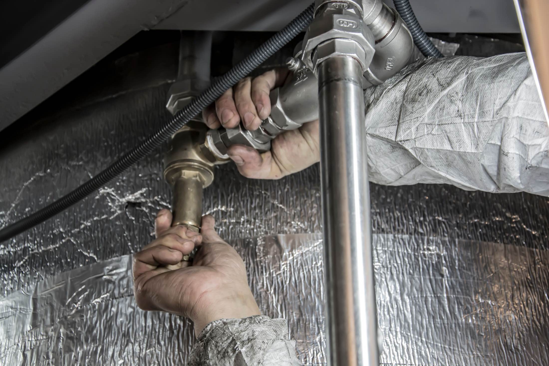 Gloved hands tightening a fitting on a copper supply line