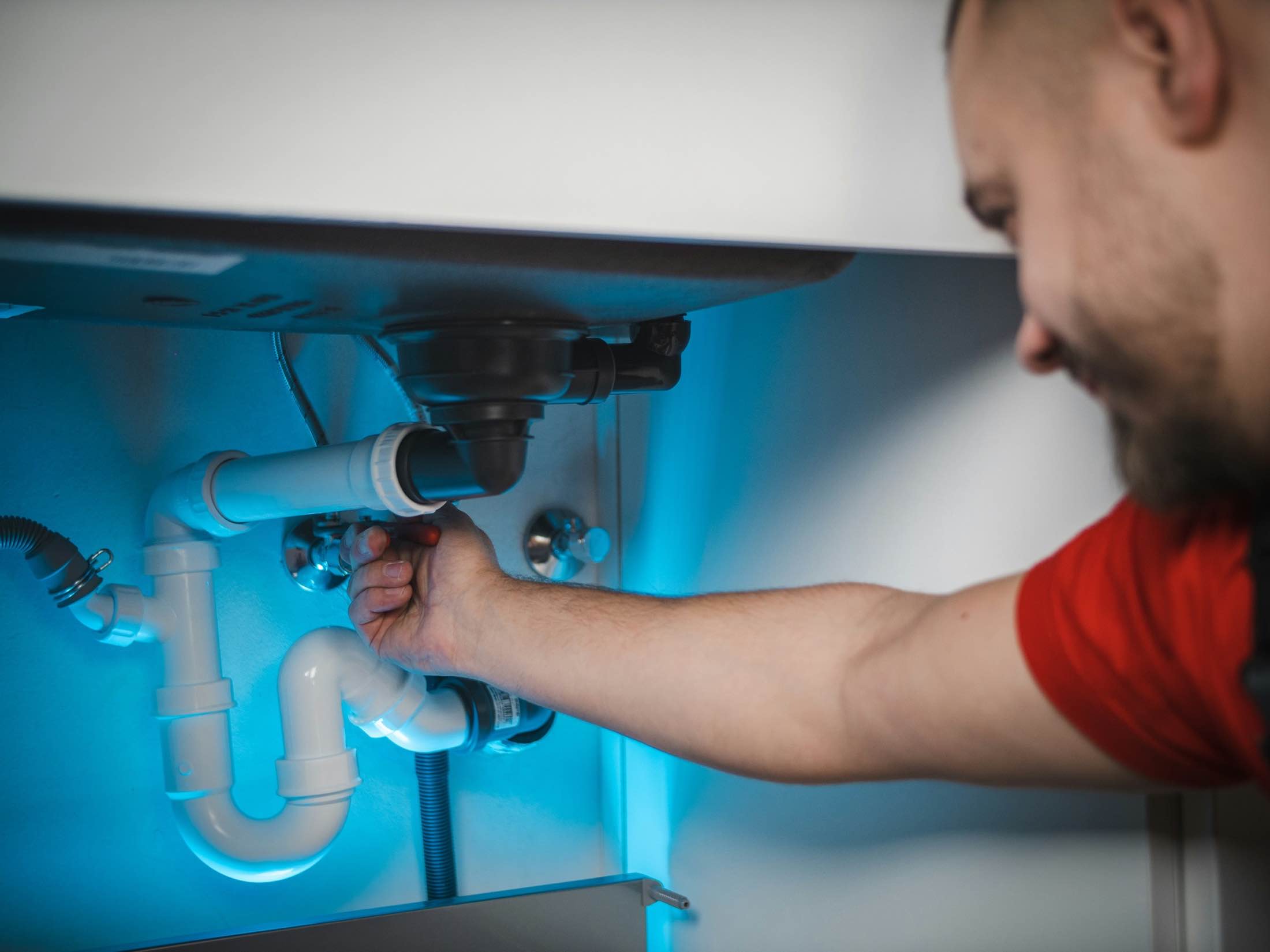 Hands fitting a white drain trap beneath a basin